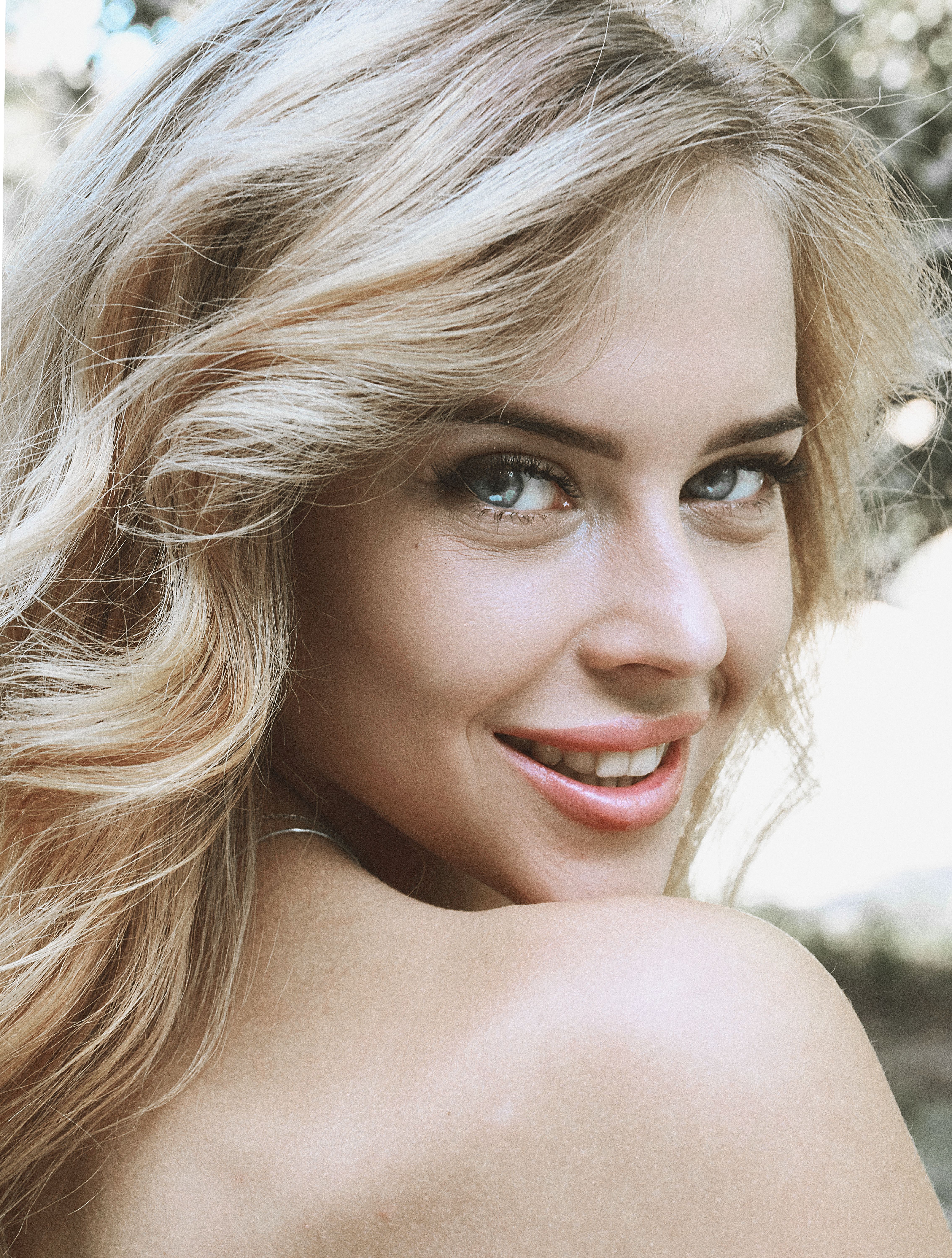 Close-up portrait of a smiling blonde woman outdoors with a natural background.