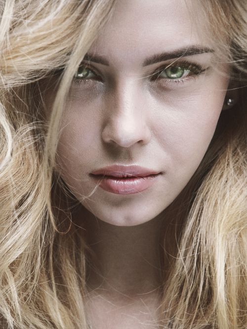 Free Intense close-up portrait of a blonde woman with striking green eyes and soft expression. Stock Photo