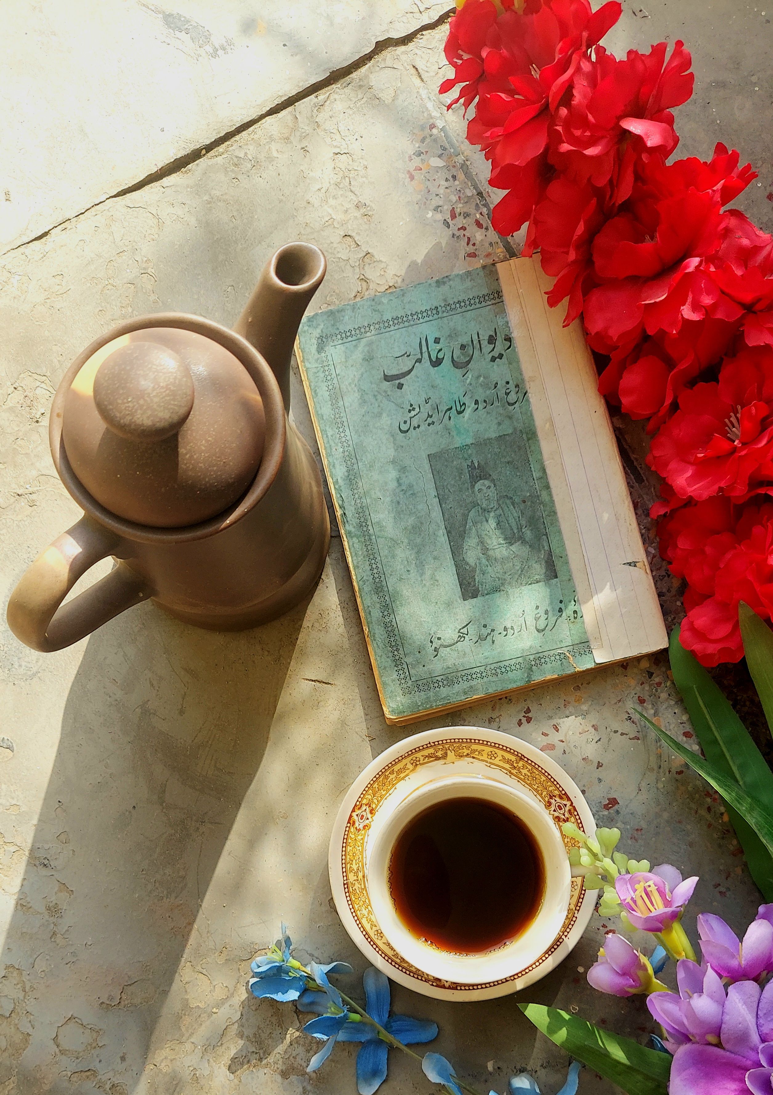 Elegant flat lay photo with a teapot, book, and vibrant flowers in soft lighting.