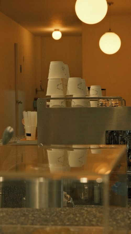 Free Warm-toned café interior featuring stacked disposable cups and a coffee counter. Stock Photo