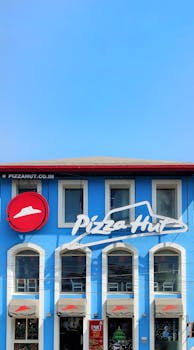 Blue facade of Pizza Hut with clear sky, showcasing urban fast food architecture.