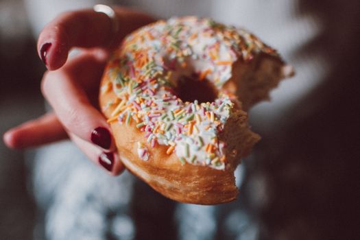 Close-up of a partially eaten doughnut with colorful sprinkles held in hand.