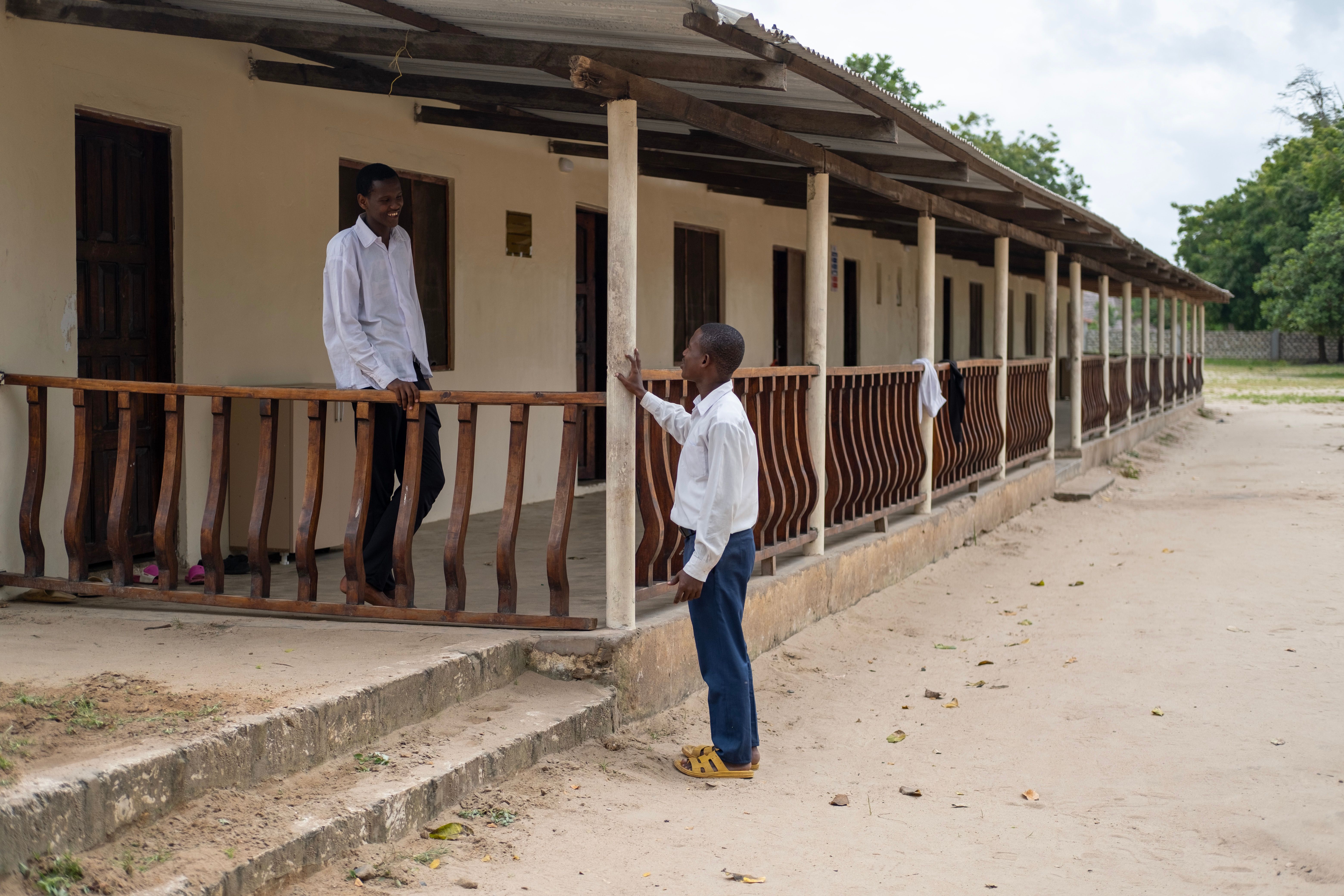 Two African men in conversation on a rustic porch in a rural village setting, showcasing community and connection.