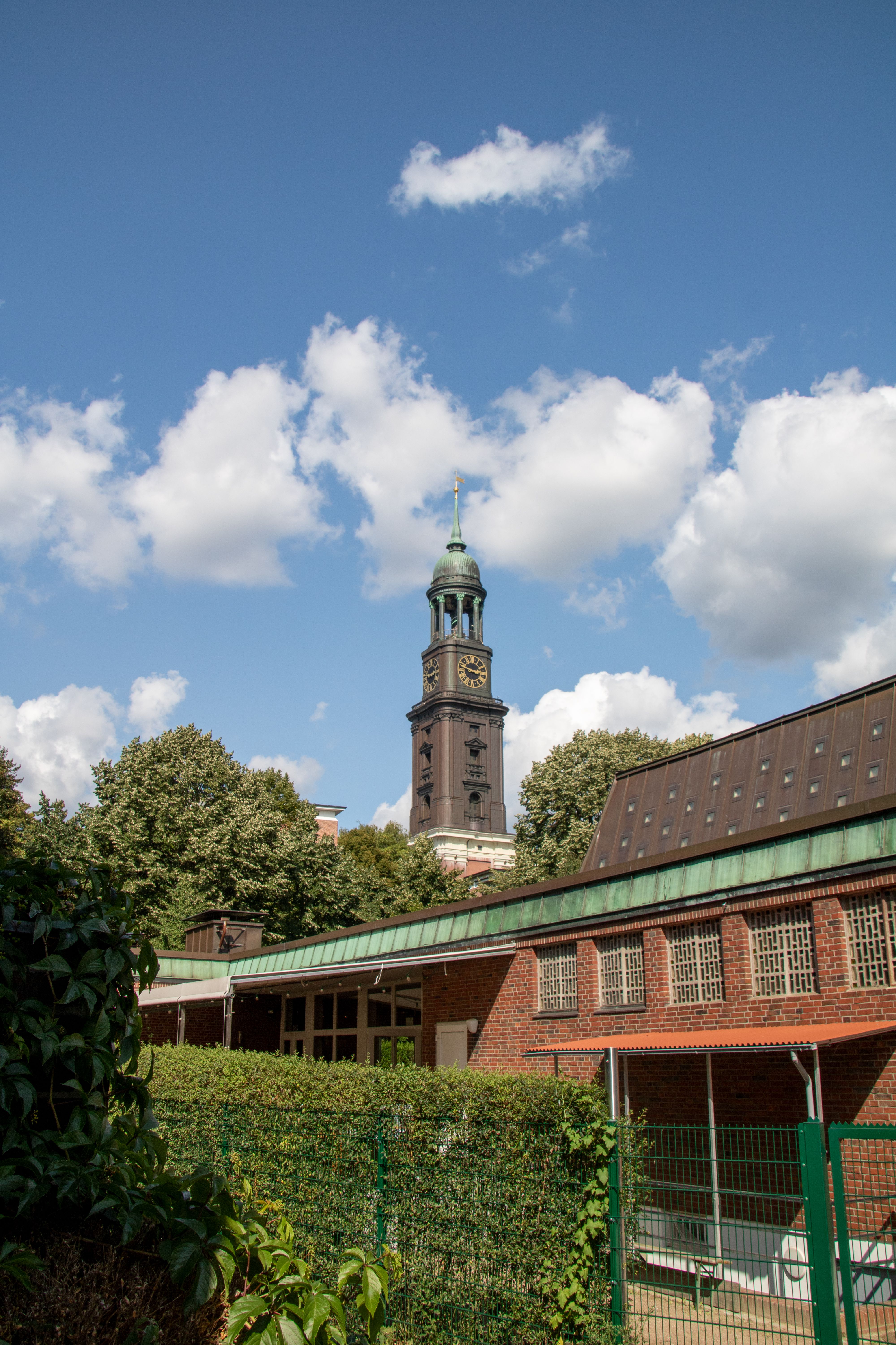 View of St. Michael's Church tower rising above buildings and trees in Hamburg on a sunny day.