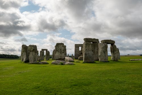 Free A historic view of Stonehenge with dramatic clouds and green fields, showcasing British heritage. Stock Photo