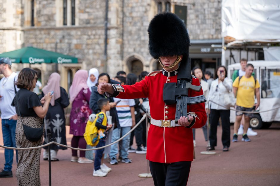 British soldier in traditional uniform stands on duty at Windsor Castle, surrounded by tourists.