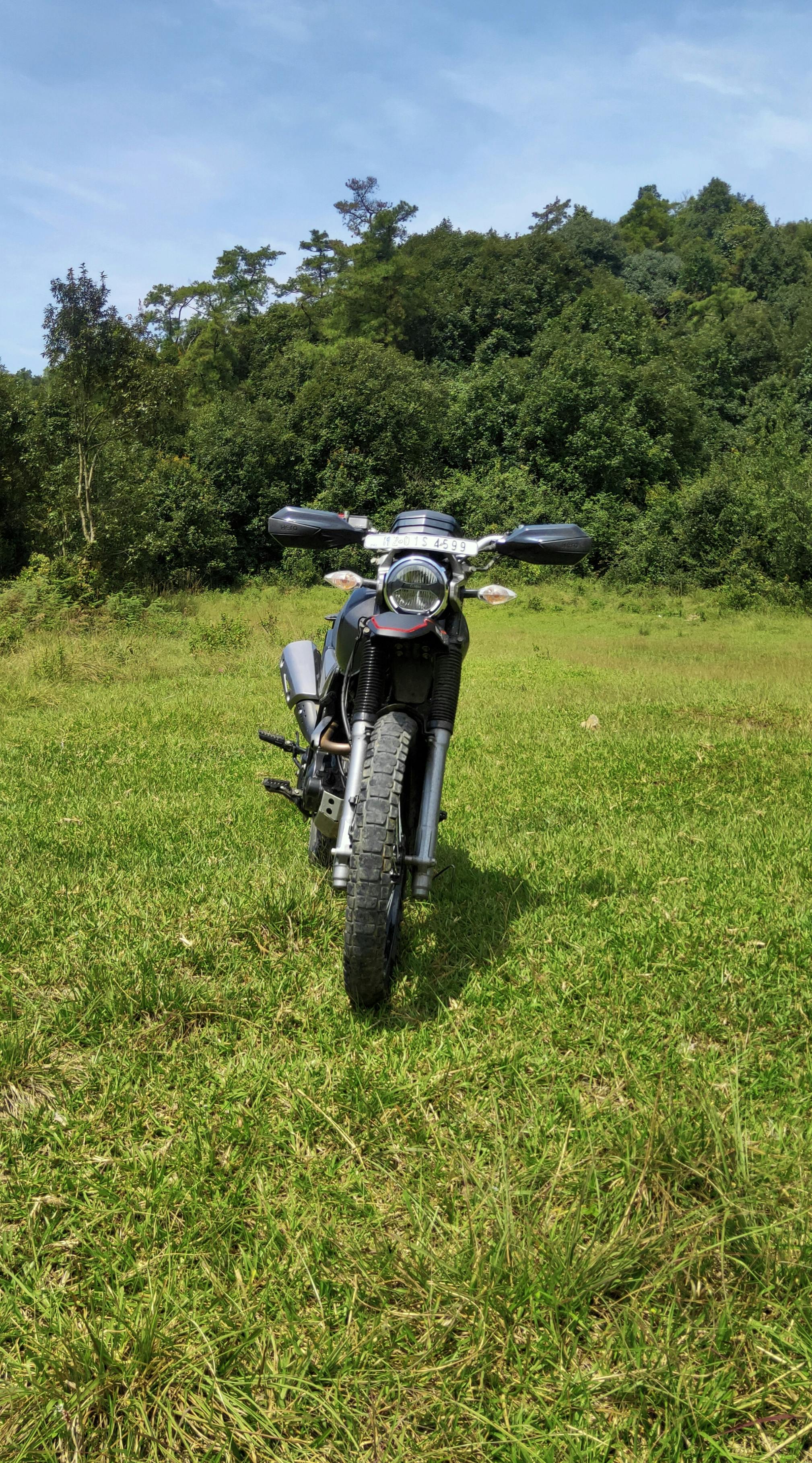 Off-road motorcycle in a lush green meadow with dense trees in Shillong, India.