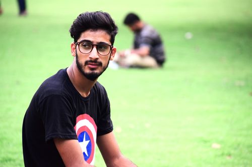 Free Portrait of a young man with eyeglasses sitting in a sunny park. Stock Photo