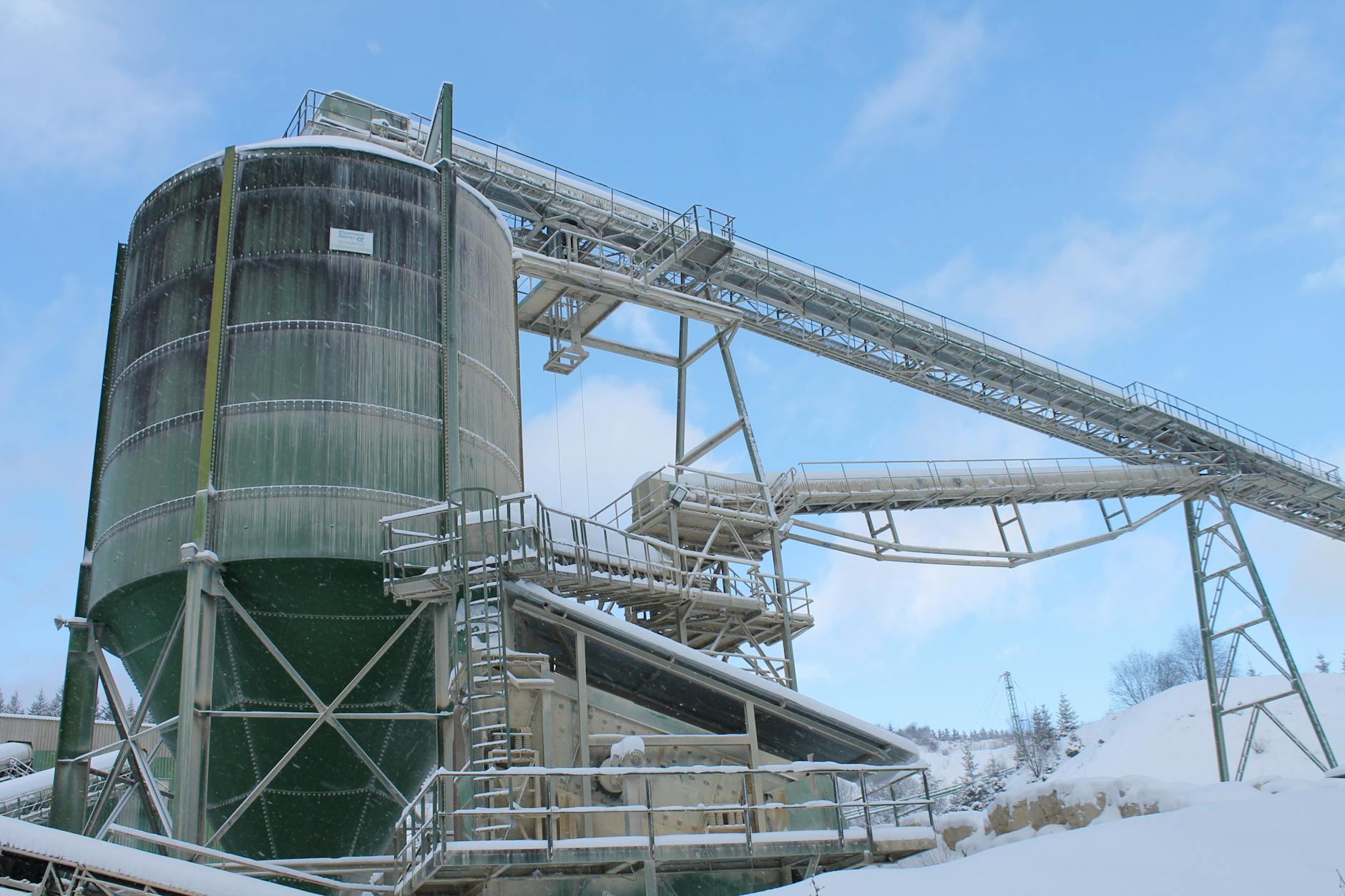 A snow-covered industrial plant with silo and machinery under a blue sky.