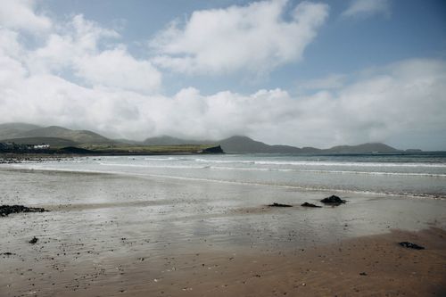 Free Beautiful coastal view with waves and mountains under a partly cloudy sky. Stock Photo