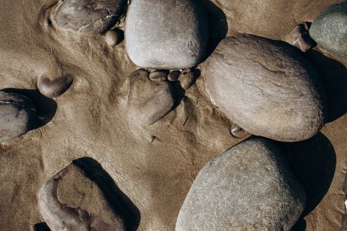 Free Detailed close-up of smooth stones resting on wet sand, capturing natural textures and earthy tones. Stock Photo