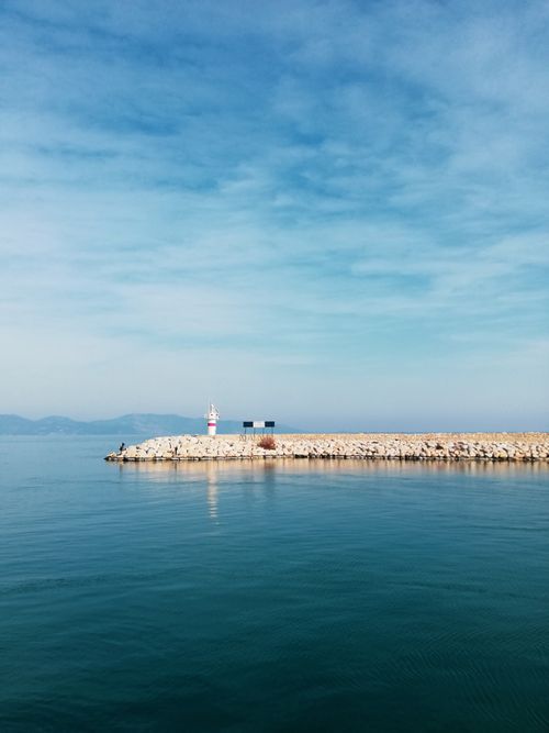 Free Peaceful seascape featuring a lighthouse on a rocky pier with calm water and clear skies. Stock Photo