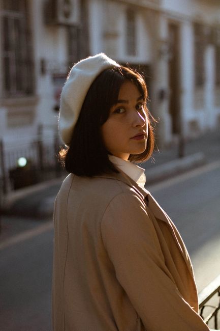 Stylish young woman in a trench coat and beret walking through the streets of Baku, Azerbaijan, with an urban backdrop.
