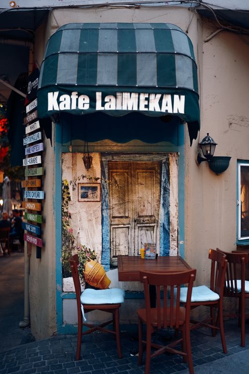 Free A cozy urban café corner with inviting wooden chairs and a rustic door under an awning. Stock Photo