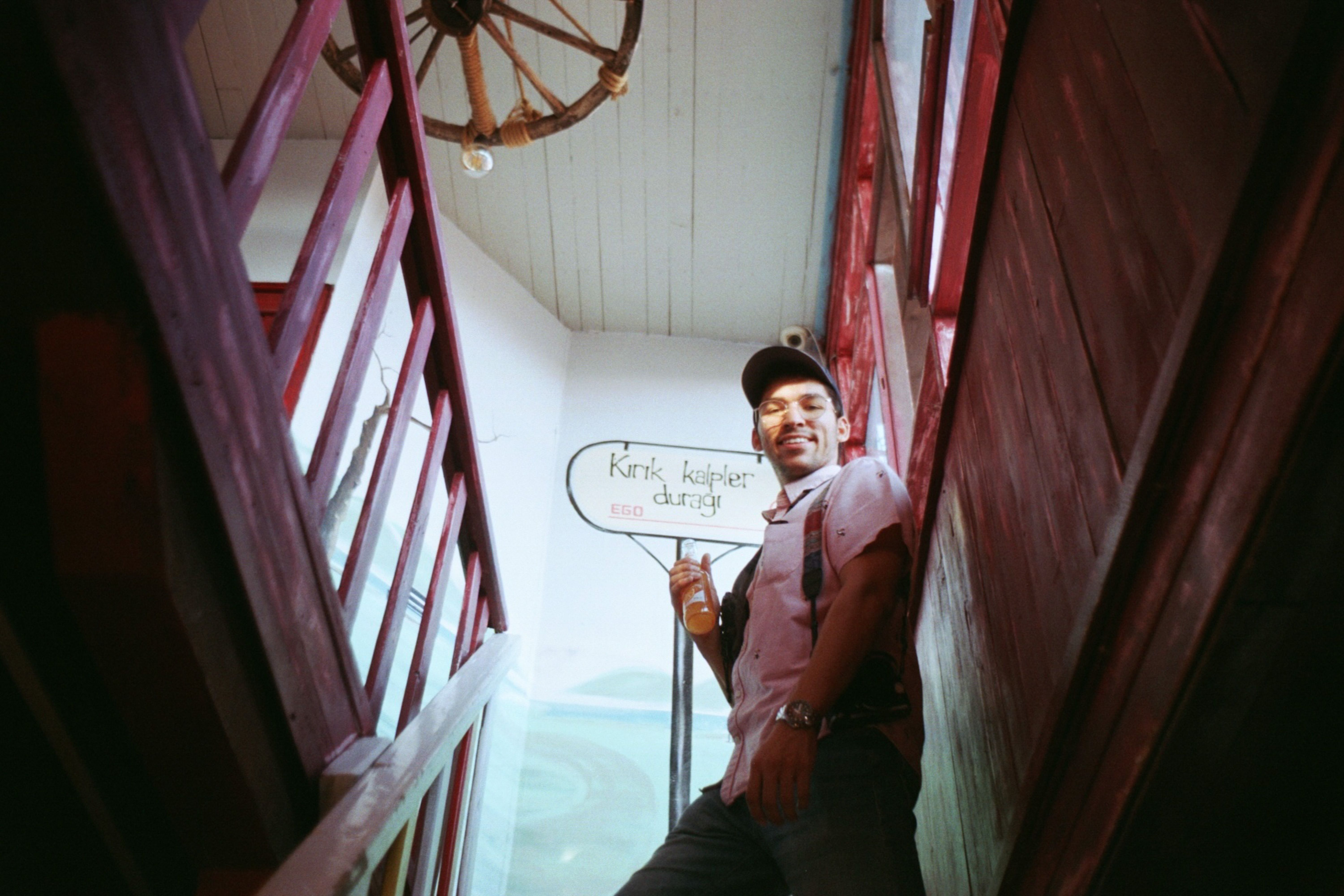 Smiling man with drink in hand on wooden staircase indoors, low angle view.