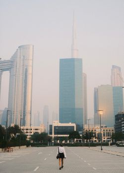 A woman walking on an empty street amidst towering skyscrapers in Dubai, UAE.