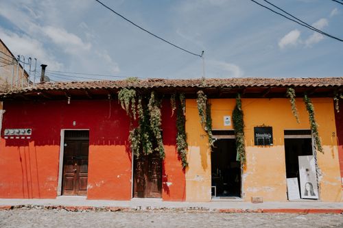 Free Vibrant red and yellow townhouses with hanging plants under a blue sky. Stock Photo