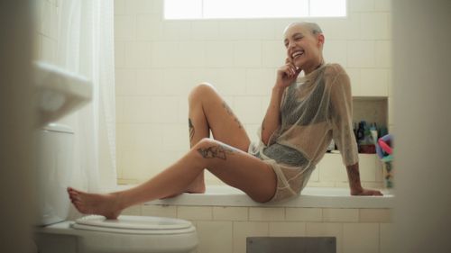 Free Joyful bald woman with tattoos relaxing in a bathroom, smiling brightly. Stock Photo