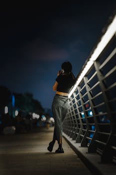 Back view of woman talking on phone by an urban railing at night.