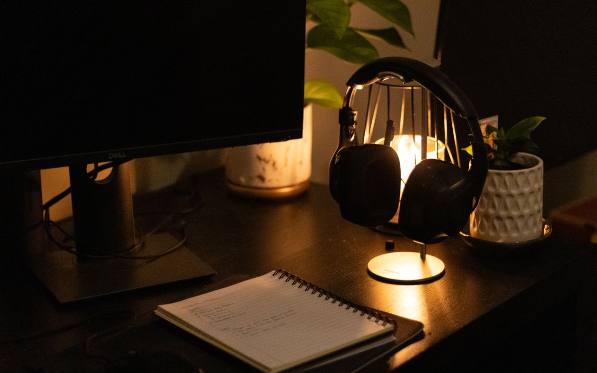 Warmly lit desk with monitor, headphones, and notebook for a cozy workspace vibe.