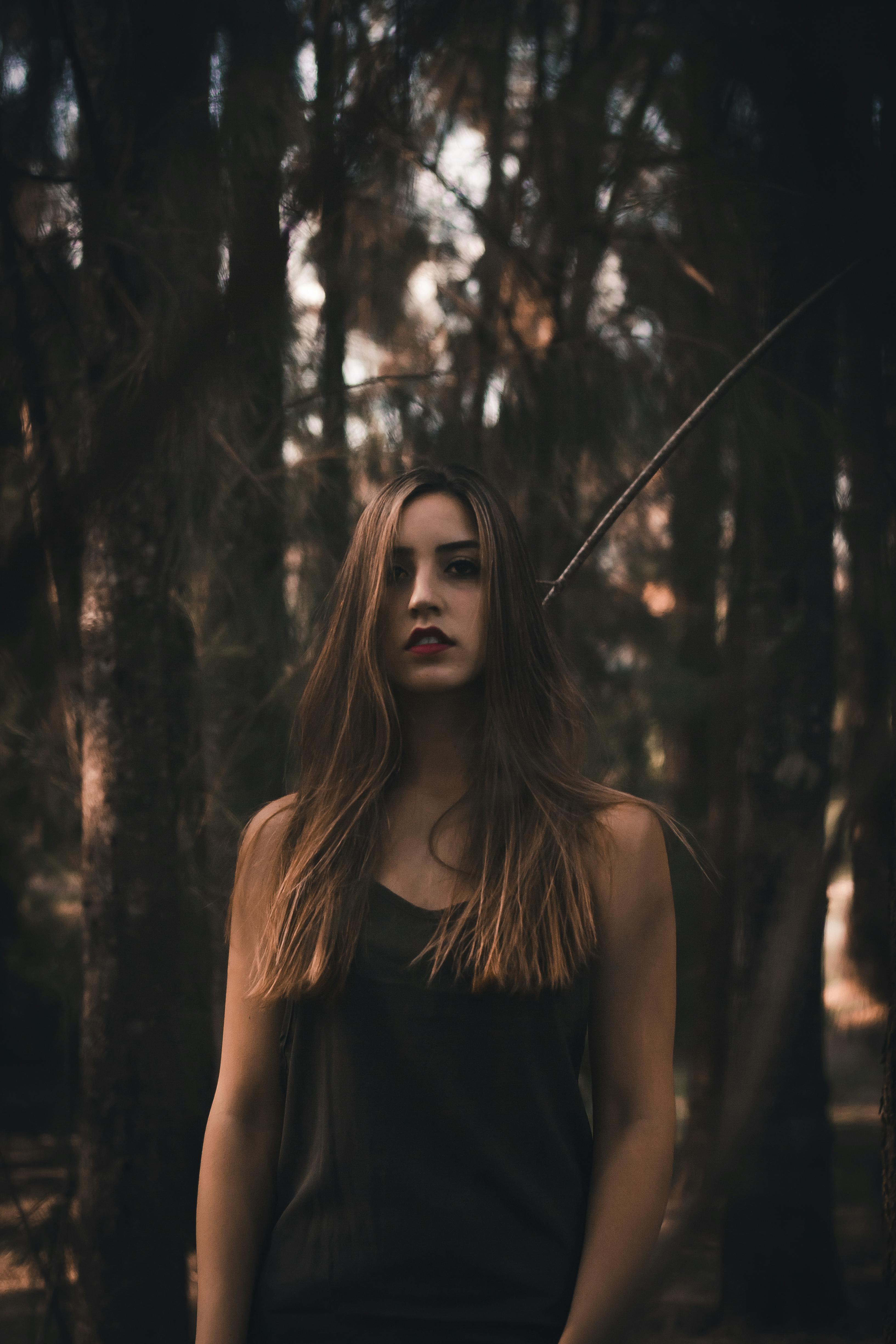 一幅艺术肖像中，一位长发女人站在幽暗阴森的森林里