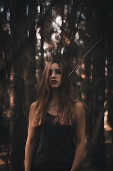 一幅艺术肖像中，一位长发女人站在幽暗阴森的森林里