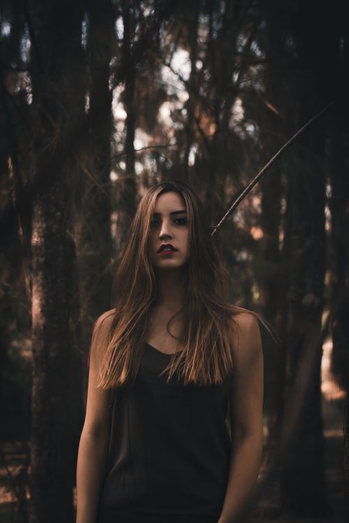 Free Artistic portrait of a woman standing in a dark, moody forest with long hair. Stock Photo