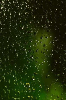 Close-up of raindrops on glass with a blurred green backdrop, evoking serenity.