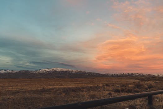 Breathtaking view of a sunset over snow-capped mountains and an open field. Perfect for nature lovers.