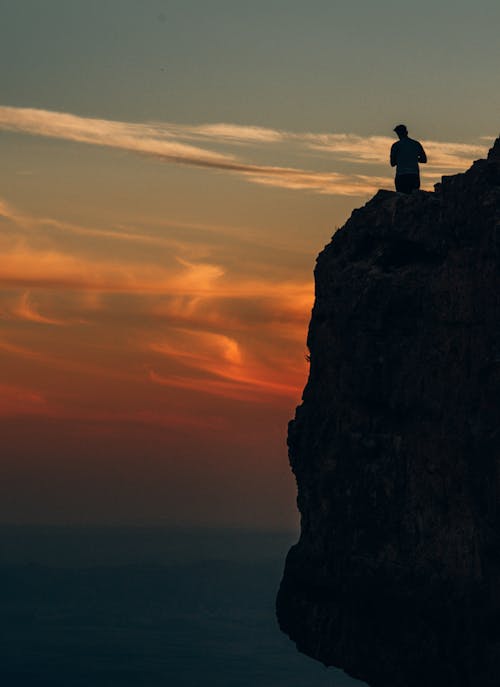 A man standing on a cliff looking sunset.