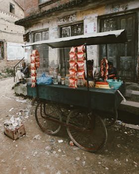 A street vendor's cart in an urban area with packaged goods and surrounding litter.
