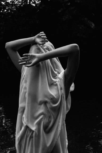 A moody black and white image of a woman in flowing fabric with obscured face, adding a sense of mystery.
