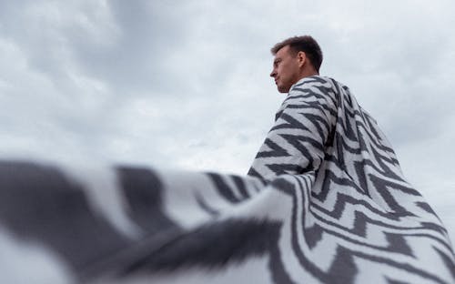 Man Covered with a Blanket Standing Against a Cloudy Sky