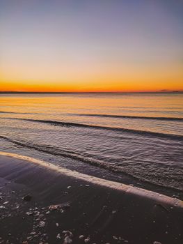 A calm coastal scene with gentle waves during a vibrant sunset, offering a tranquil and warm atmosphere.