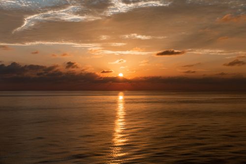 Free Beautiful warm-toned sunset over a calm ocean, capturing the serene beauty of dusk. Stock Photo