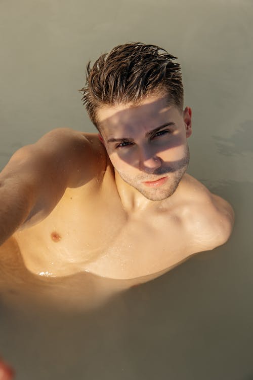 A shirtless man is taking a selfie in the water