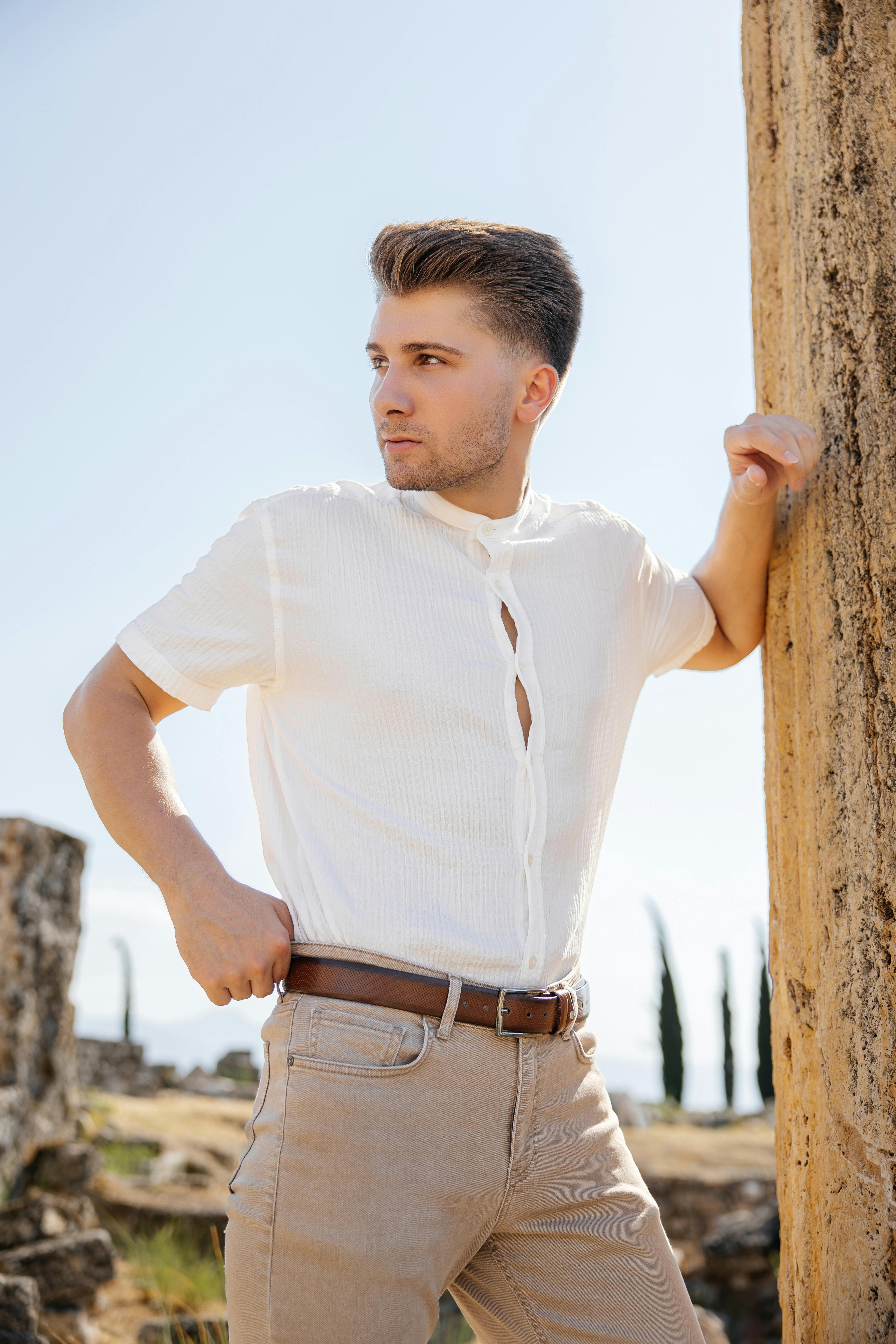 a man in a white shirt and tan pants leaning against a pillar