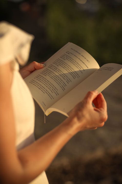 Free Close-up of a woman reading a book outdoors with natural sunlight, emphasizing leisure and relaxation. Stock Photo