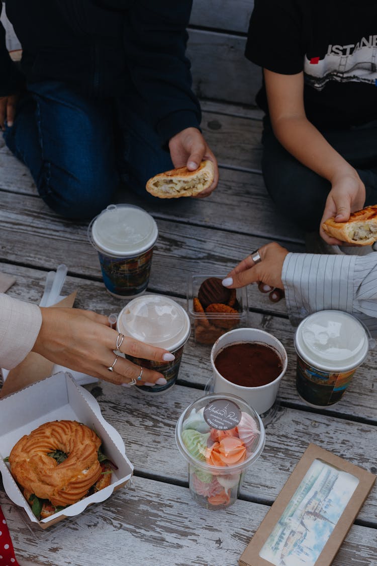 Hands Of People Eating Takeout Food On Wooden Jetty