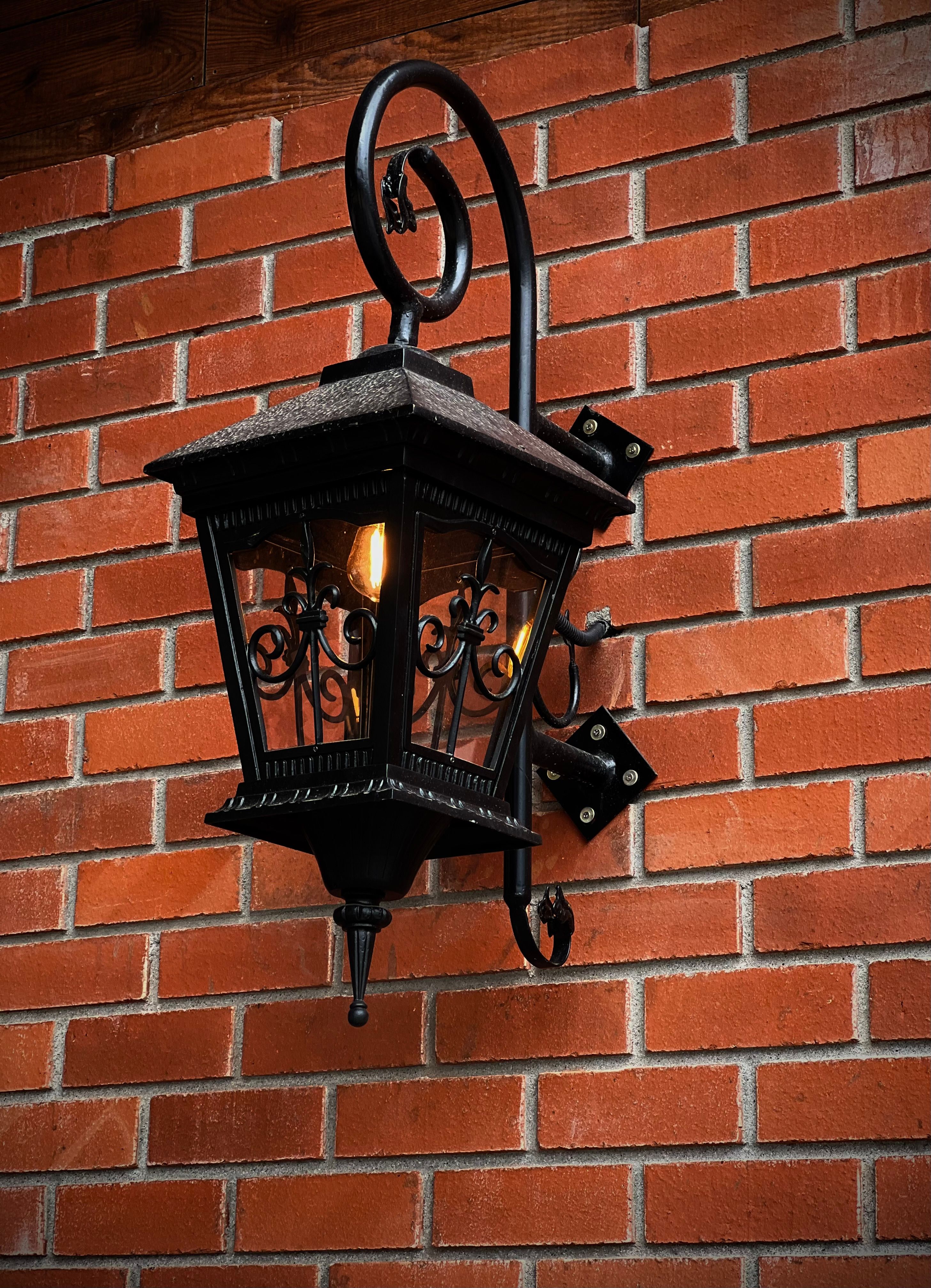 A classic metal lantern with intricate designs attached to a red brick wall, illuminated warmly.