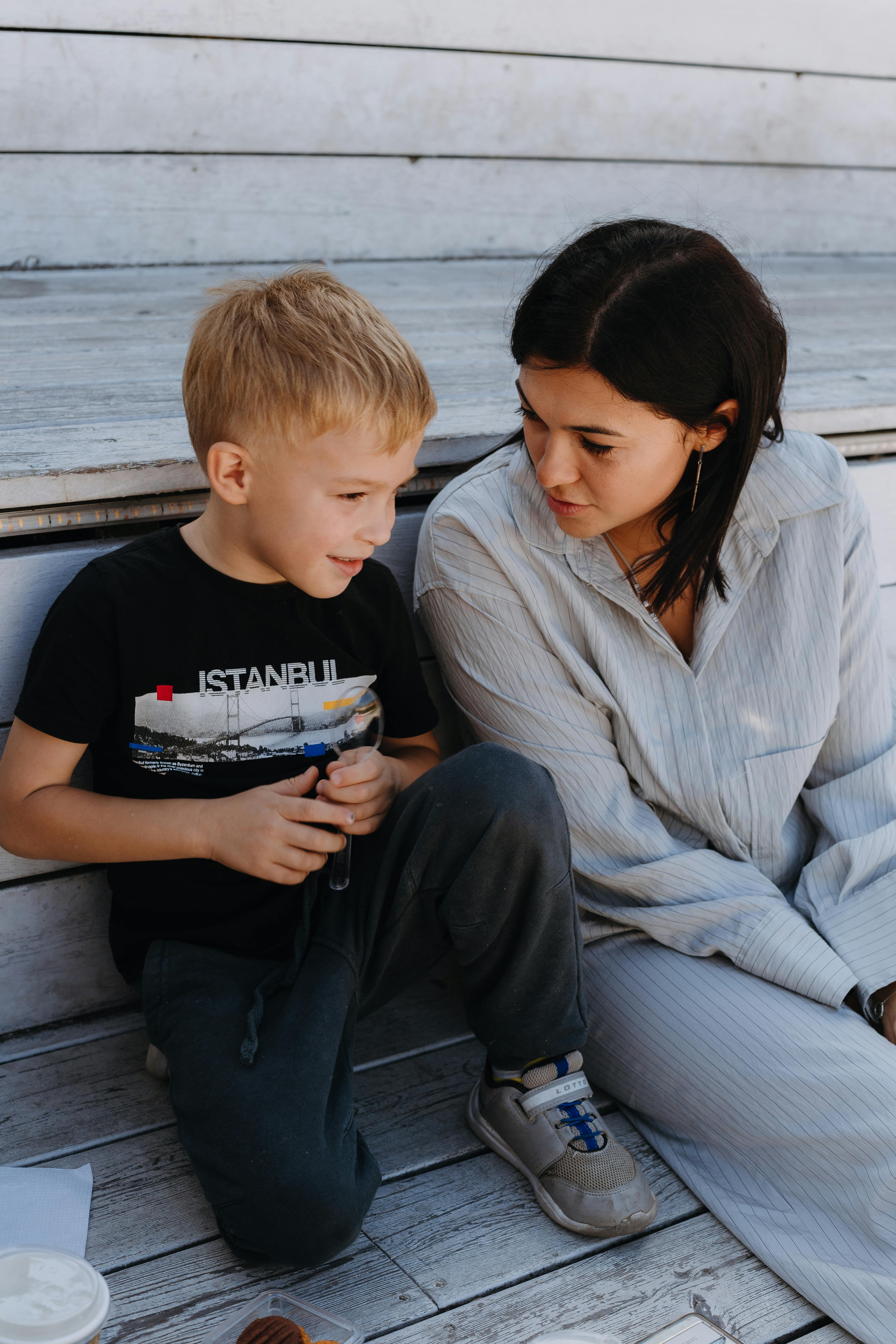 Mother and young son sharing a heartfelt conversation while sitting on wooden steps outdoors