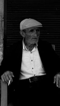 An elderly man with deep features enjoys a cigarette, captured in moody black and white.