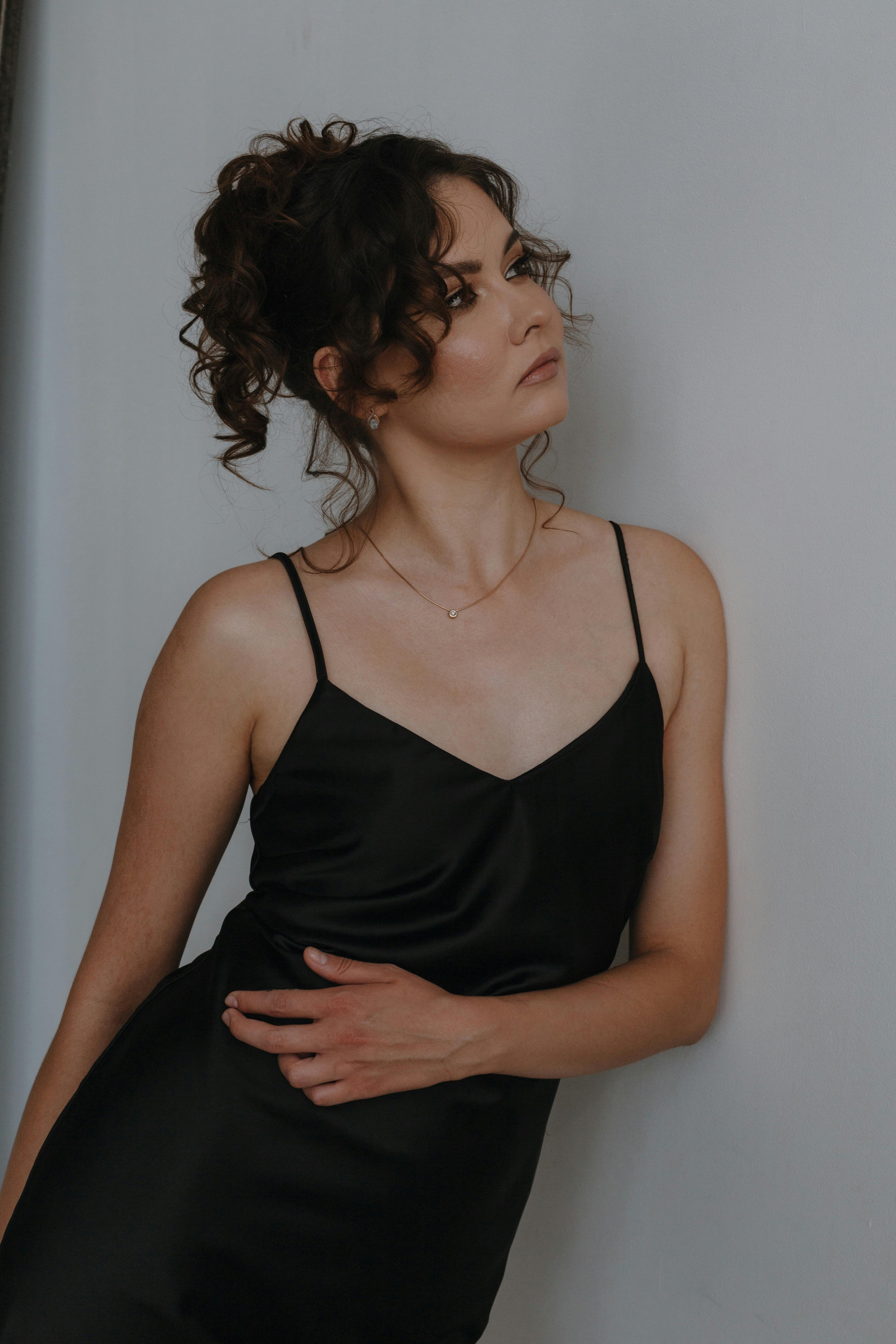 Stylish portrait of a woman in a black dress with curly hair, showcasing elegance and modern fashion.