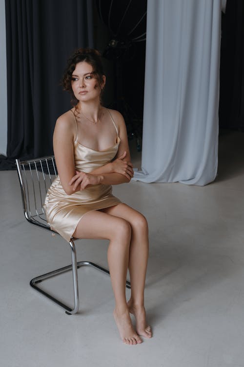 Barefoot Woman in Spaghetti Strap Dress Sitting on Model Metal Chair