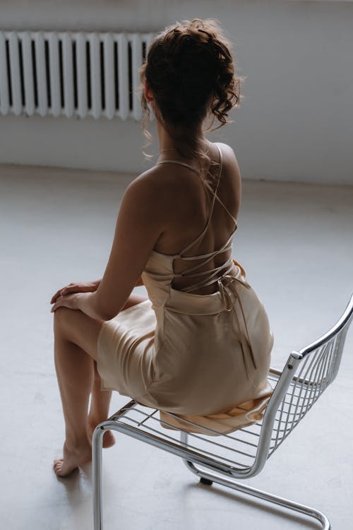 Sitting on Modern Chair Woman in Spaghetti Strap Dress Tied on Back
