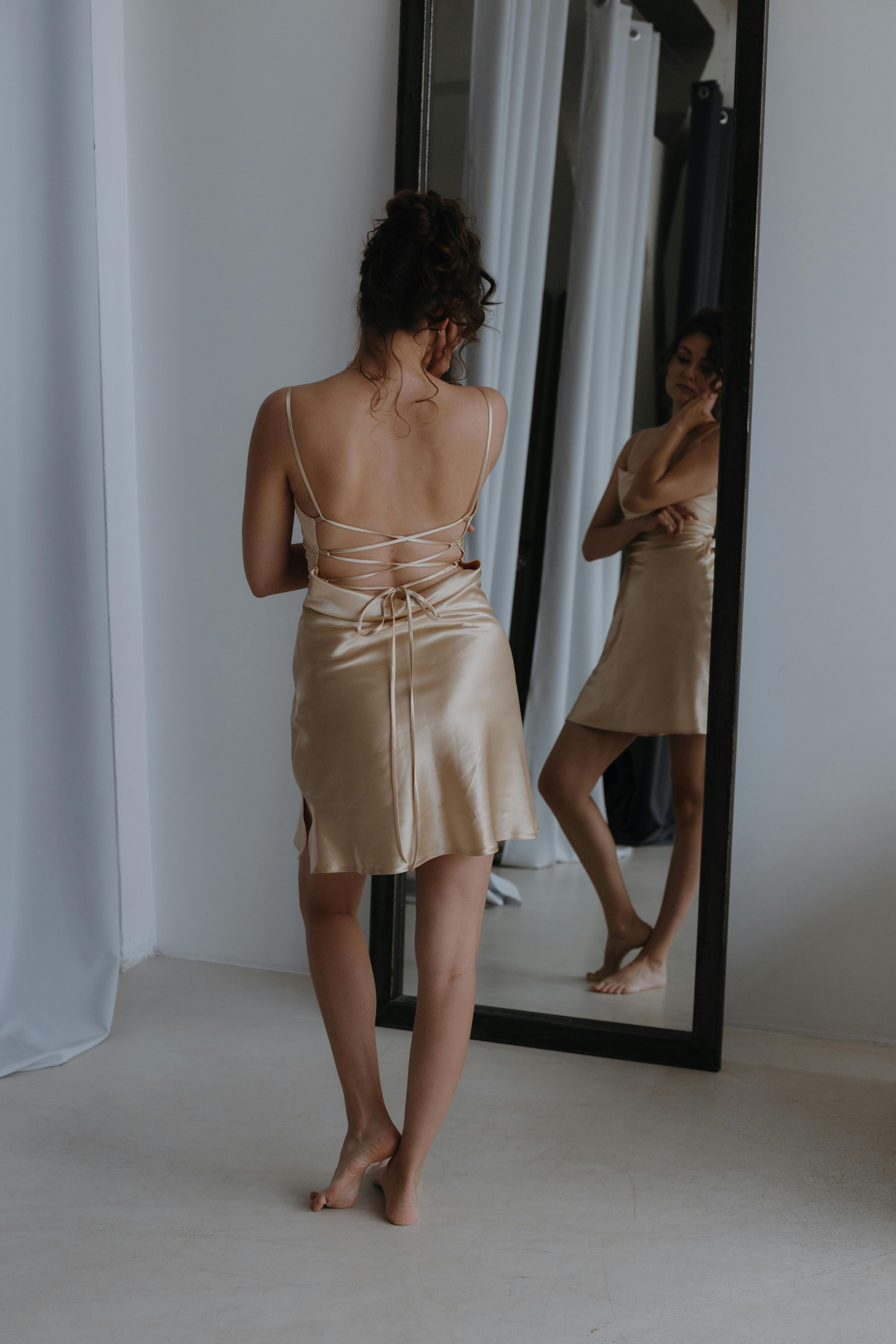 Brunette Woman in Champagne Color Backless Slip Dress Posing in front of  Mirror · Free Stock Photo