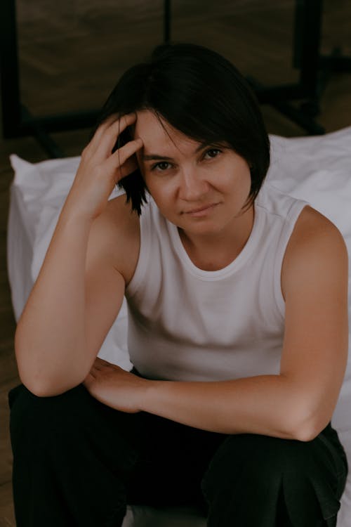 Short Haired Brunette Woman in White Tank Top Sitting on a Bed