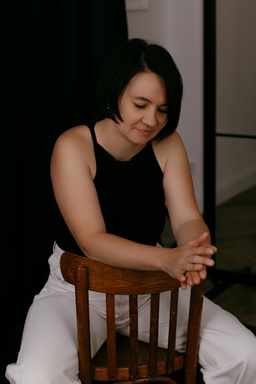  Model in a Black Tank Top and White Pants Sitting Backwards on a Chair