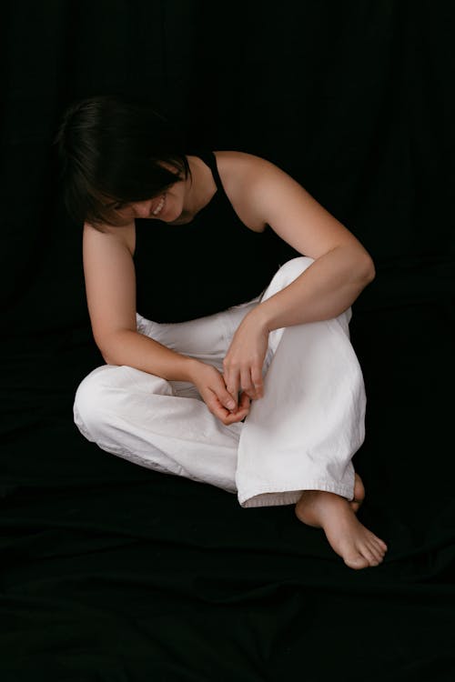 Model in a Black Tank Top and White Pants Sitting on the Floor