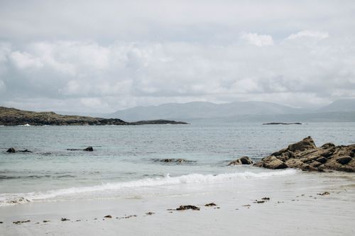 Free Serene sandy beach with gentle waves and distant rocky coastline under a cloudy sky. Stock Photo